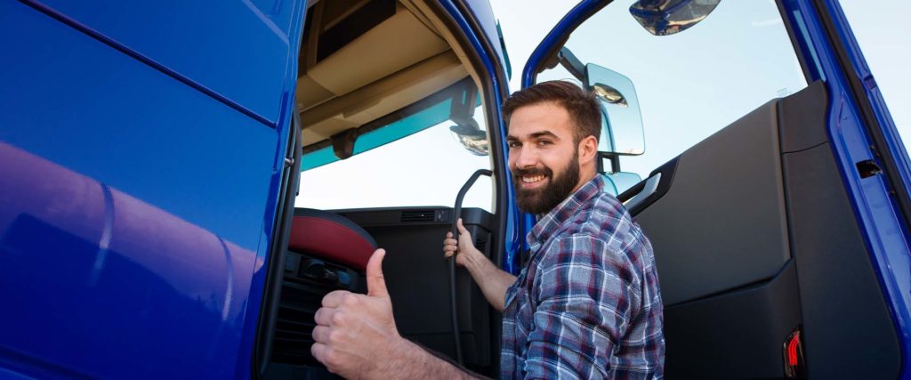 Smiling trucker gives a thumbs up in from of his blue semi truck